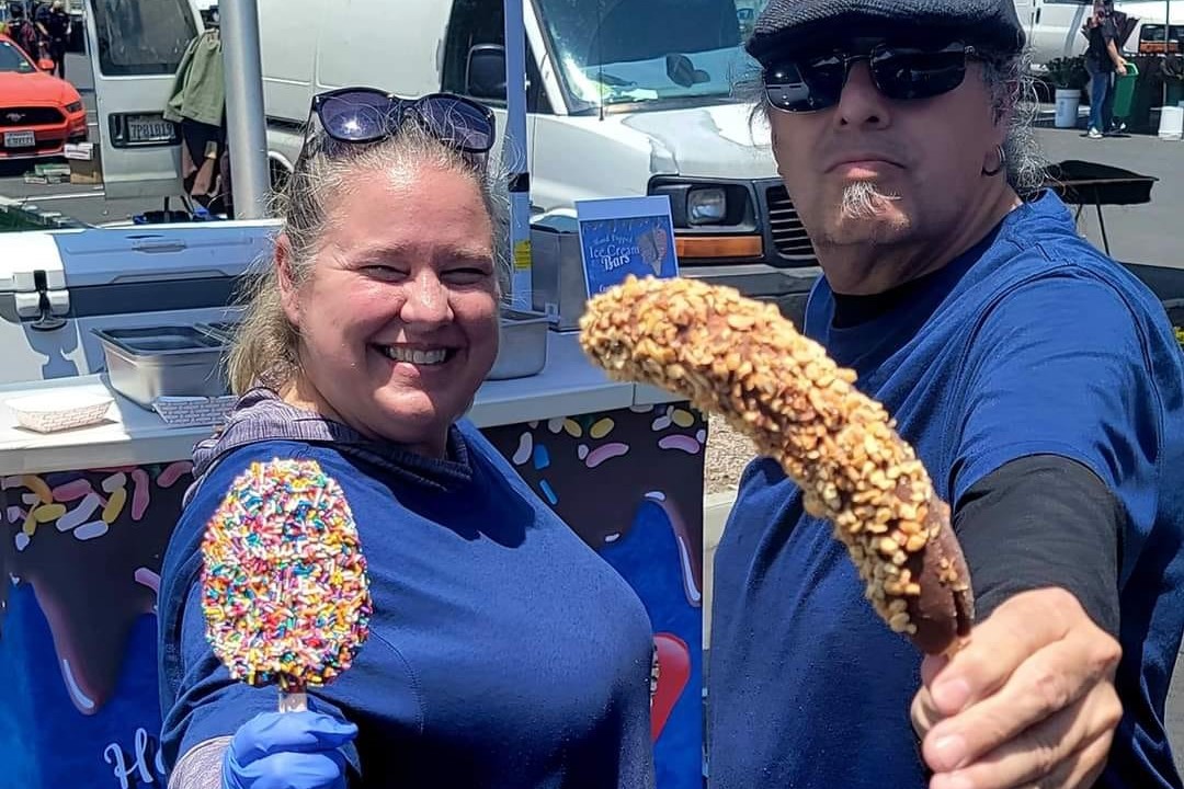 A man and woman holding a frozen banana and ice cream bar.