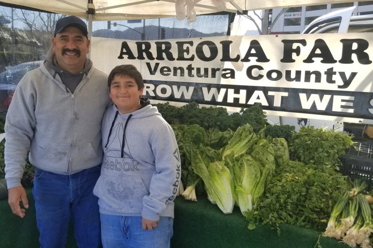 Father and son farmers in front of produce.